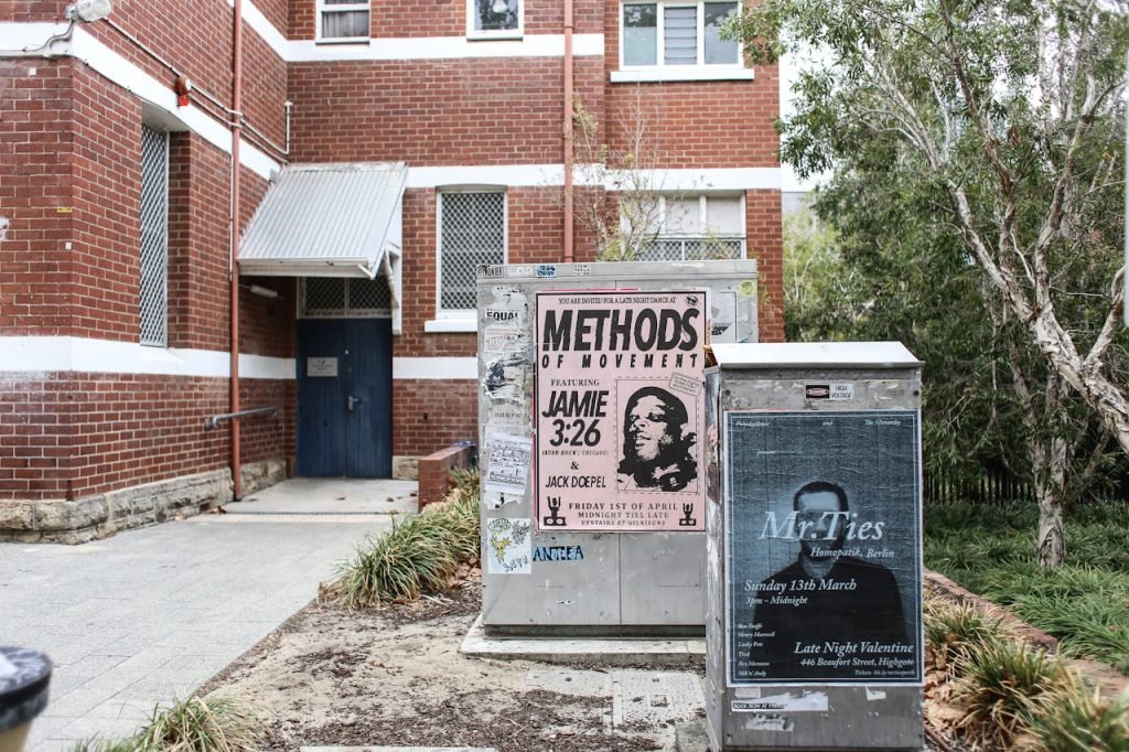 Corner view of a brick building with urban posters and greenery.