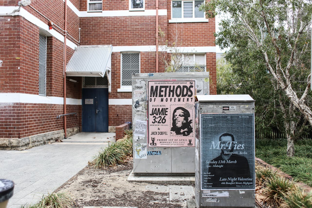 Corner view of a brick building with urban posters and greenery.